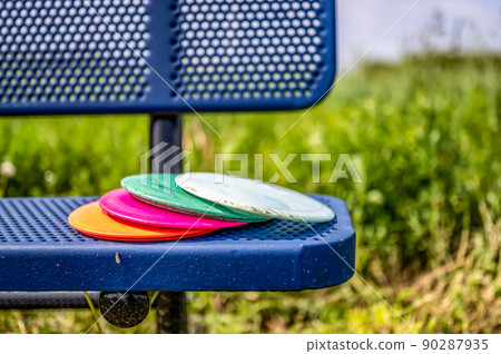 Pile of discs resting on a bench in the golf course park Pile of discs resting on a bench in the golf course park 90287935