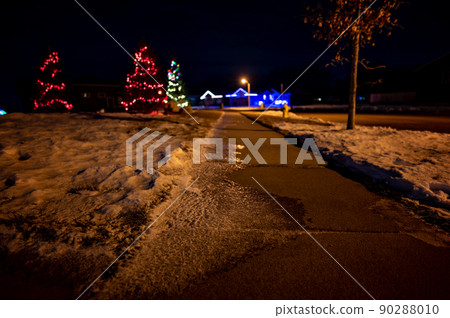 Ice and snow on a sidewalk at night with streetlight reflecting off the slick surface. 90288010
