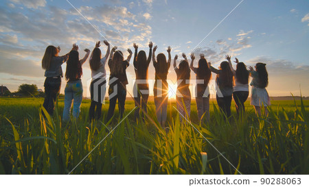 Silhouette of friends of 11 girls waving their hands at sunset in the field. Silhouette of friends of 11 girls waving their hands at sunset in the field. 90288063