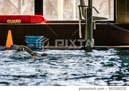 Youth swimming lesson in indoor pool. Swimmers backlit and silhouette with light reflecting off of water surface. 90288076