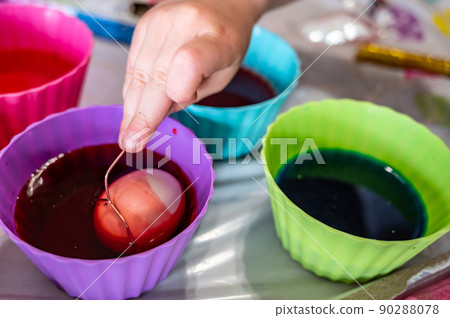 Cups of dye with an egg being lowered in for Easter decorations 90288078