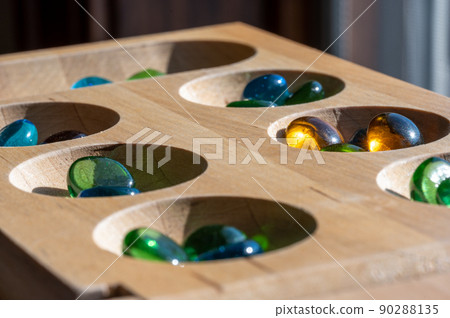 Selective focus on glass beads on a wooden mancala board 90288135