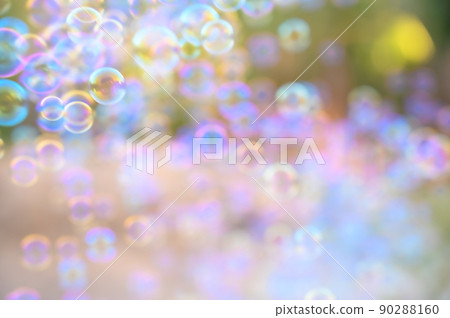 Abstract blurred of rainbow soap bubbles from the bubble blower flying on green grass. spring or summer season background. symbol of childhood. bokeh background. Abstract blurred of rainbow soap bubbles from the bubble blower flying on green grass. spring or summer season background. symbol of childhood. bokeh background. 90288160