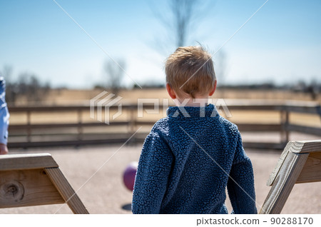 Child waiting along fence for next round of gaga ball in a school playground. Child waiting along fence for next round of gaga ball in a school playground. 90288170