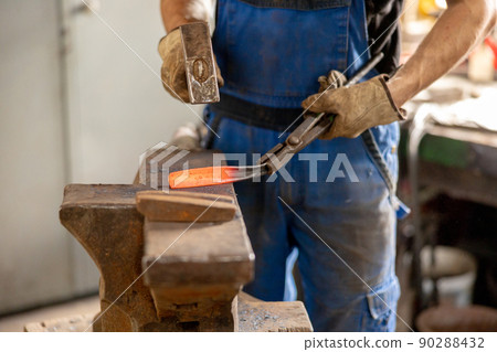Close up view of heated metal and anvil. The blacksmith in the production process of metal products handmade in the forge. Blacksmith forging metal with a hammer. Metal industry, old profession. Close up view of heated metal and anvil. The blacksmith in the production process of metal products handmade in the forge. Blacksmith forging metal with a hammer. Metal industry, old profession. 90288432