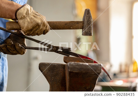 Close up view of heated metal and anvil. The blacksmith in the production process of metal products handmade in the forge. Blacksmith forging metal with a hammer. Metal industry, old profession. Close up view of heated metal and anvil. The blacksmith in the production process of metal products handmade in the forge. Blacksmith forging metal with a hammer. Metal industry, old profession. 90288435