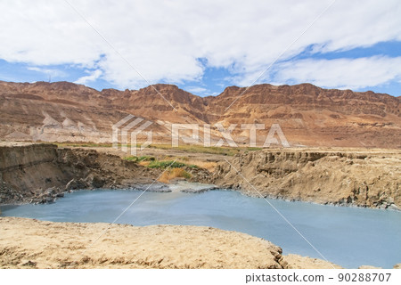 Sinkhole filled with turquoise water, near Dead Sea coastline. Hole formed when underground salt is dissolved by freshwater intrusion, due to continuing sea-level drop.  90288707