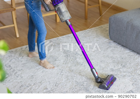 Woman using a cordless vacuum cleaner in the room 1 90290702