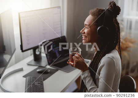 Side view of cheerful young female wearing headphones and programming on computer Side view of cheerful young female wearing headphones and programming on computer 90291236