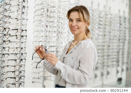 Beautiful woman chooses glasses standing near a showcase in modern ophthalmic store 90291244