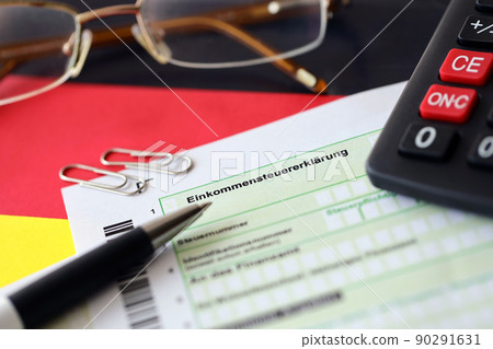 German income tax return form with pen and european euro money bills lies on flag close up. Taxpayers in Germany using euro currency to pay taxes 90291631
