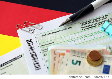 German income tax return form with pen and european euro money bills lies on flag close up. Taxpayers in Germany using euro currency to pay taxes 90292163