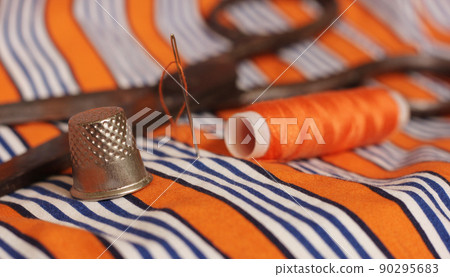 Orange Thread and Thimble on Orange and White Striped Fabric 90295683