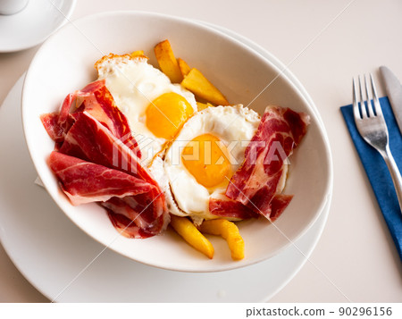 Breakfast of fried eggs with slices of delicious bacon and French fries Breakfast of fried eggs with slices of delicious bacon and French fries 90296156