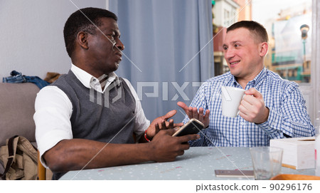 Men enjoying conversation at home, using phone Men enjoying conversation at home, using phone 90296176