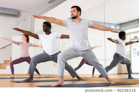 Man practising warrior two pose with group in gym 90296338