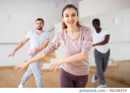 Young woman practicing vigorous dance movements with group 90296454