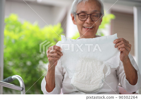 Happy smiling asian senior woman showing disposable diaper for adult,looking at nappy pamper with satisfaction,old elderly patient with urinary incontinence,consumer goods,health care concept 90302264