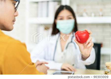 Asian expertise cardiologist doctor showing a beautiful red heart shape to the camera, concept of health care and cardiology medication. 90303009