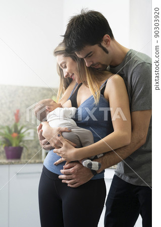 Mother breastfeeding her son in the kitchen with his father by her side 90303920