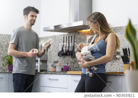 mother and father preparing a feeding bottle for their newborn in the kitchen 90303921