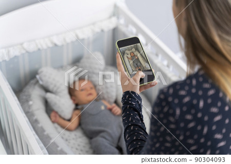 Young mother taking a picture to her newborn baby in the cradle Young mother taking a picture to her newborn baby in the cradle 90304093