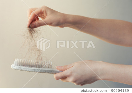 Hair loss. Female hand pulls out a clump of hair from a comb. Close-up. The concept of alopecia and trichology 90304189