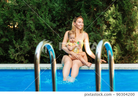 Summer vacation. A plus sized woman sitting by the pool with little daughter. Family vacation Summer vacation. A plus sized woman sitting by the pool with little daughter. Family vacation 90304200