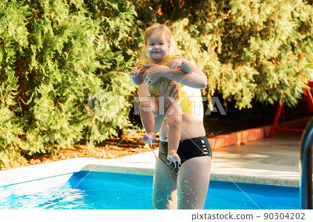 A mother plays with her little daughter in the pool. Summertime 90304202