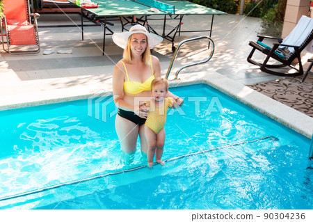 Summer vacation. Happy plus sized woman in bikini holding little cute girl and learnng swimming in a pool. Top view 90304236