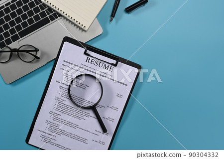 Top view laptop computer, magnifying glass and resumes applicants on blue background. Job search concept Top view laptop computer, magnifying glass and resumes applicants on blue background. Job search concept 90304332