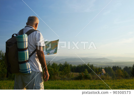 Back panoramic view of old male with gray hair wearing rucksack, looking at map in hills. Man searching route, traveling, hiking in mountains. Concept of active recretaion, 90308573