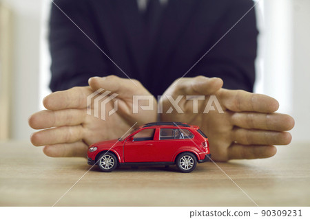 Man protecting toy car illustrating insurance, safety, protection, and warranty concepts 90309231