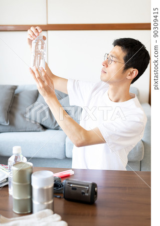 一名男子正在檢查庫存中的水的有效期並將其放在陽光下以檢查雜質等。 90309415