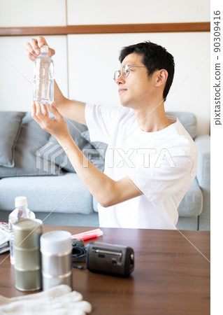 A man who is checking the expiration date of the water in the stockpile and holding it over the sunlight to check for impurities etc. 90309416
