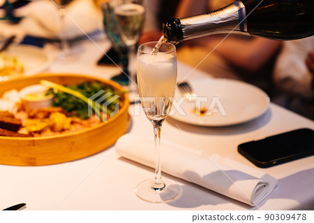 The waiter pours the champagne into the glasses. The waiter pours the champagne into the glasses. 90309478