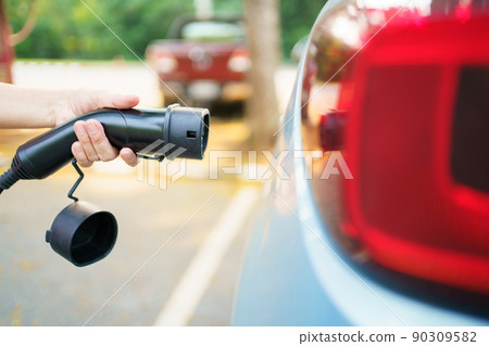 Unrecognizable Asian woman holding AC type 2 EV charging connector at EV charging station, woman preparing an EV - electric vehicle charging connector for recharge a vehicle. Unrecognizable Asian woman holding AC type 2 EV charging connector at EV charging station, woman preparing an EV - electric vehicle charging connector for recharge a vehicle. 90309582