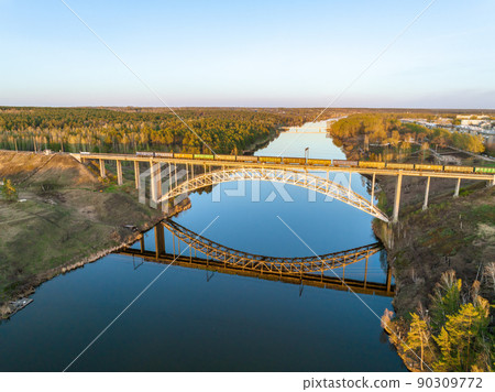 Beautiful view of the arched railway bridge across the Iset River in the city of Kamenkk-Uralsky at sunset in spring. Kamensk-Uralskiy, Sverdlovsk region, Ural mountains, Russia. 90309772