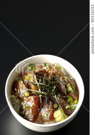 A bird's-eye view of a bowl of pickled yellowtail with chopped seaweed, all-purpose greentail, and wasabi on a black background 90310283