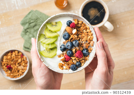 Yogurt and granola bowl with berries in female hands Yogurt and granola bowl with berries in female hands 90312439