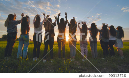 Silhouette of friends of 11 girls waving their hands at sunset in the field. Silhouette of friends of 11 girls waving their hands at sunset in the field. 90312718