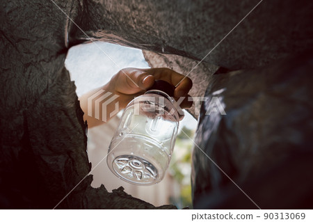 Hand putting plastic bottle in a black bag for recycling. 90313069