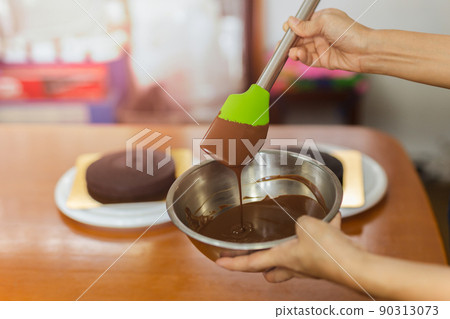 Woman mixing smooth delicious dark chocolate ganache with whisk in silver bowl. 90313073