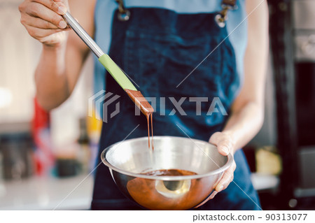 Woman mixing smooth delicious dark chocolate ganache with whisk in silver bowl. Woman mixing smooth delicious dark chocolate ganache with whisk in silver bowl. 90313077