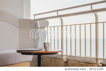 Open laptop with coffee cup on wood table on balcony with ocean view. 90313100