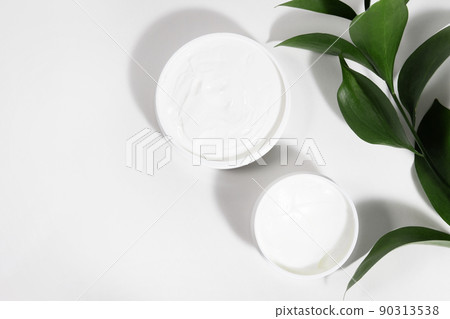 A mock up white jar of cream on a white gray background, on a white table with green leaves of a tropical plant, with hard shadows. Stylish look of the product, identity. 90313538