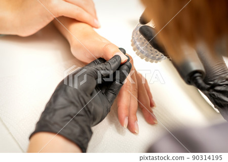 Hands of the manicure master removing dust from nails with a brush cleaning nails in a nail salon Hands of the manicure master removing dust from nails with a brush cleaning nails in a nail salon 90314195