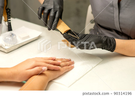 Manicure master takes out manicure tools from a kraft envelope in a nail salon Manicure master takes out manicure tools from a kraft envelope in a nail salon 90314196