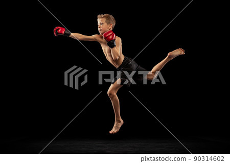 Studio shot of preschool boy, cute kid in sports shots and gloves training alone on black background. Sport, education, action, motion concept. 90314602