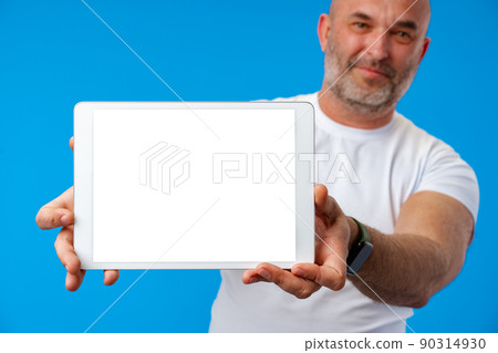 Happy caucasian middle-aged man showing tablets screen over blue background Happy caucasian middle-aged man showing tablets screen over blue background 90314930